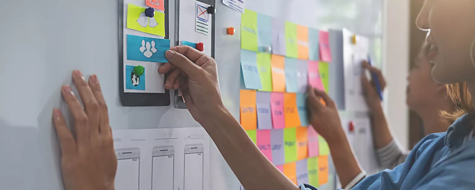 Two women standing in from of whiteboard arranging colored sticky notes 