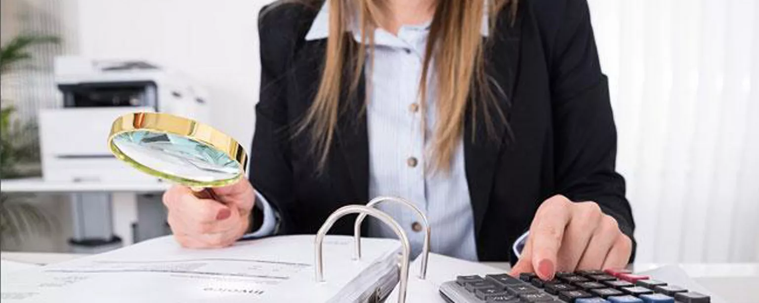 Woman with magnifying glass and calculator working in credit and collections