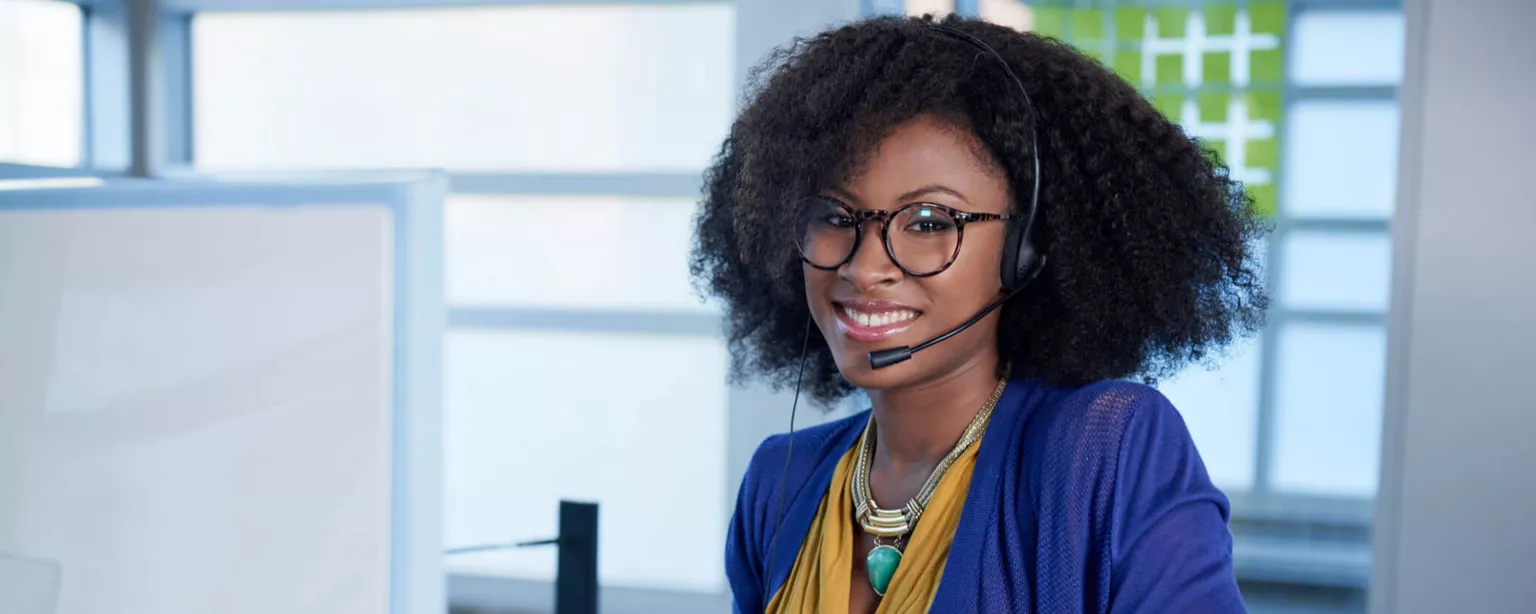 How to Become a Medical Credentialing Specialist — Woman with glasses and a headset sitting at a desk with a computer