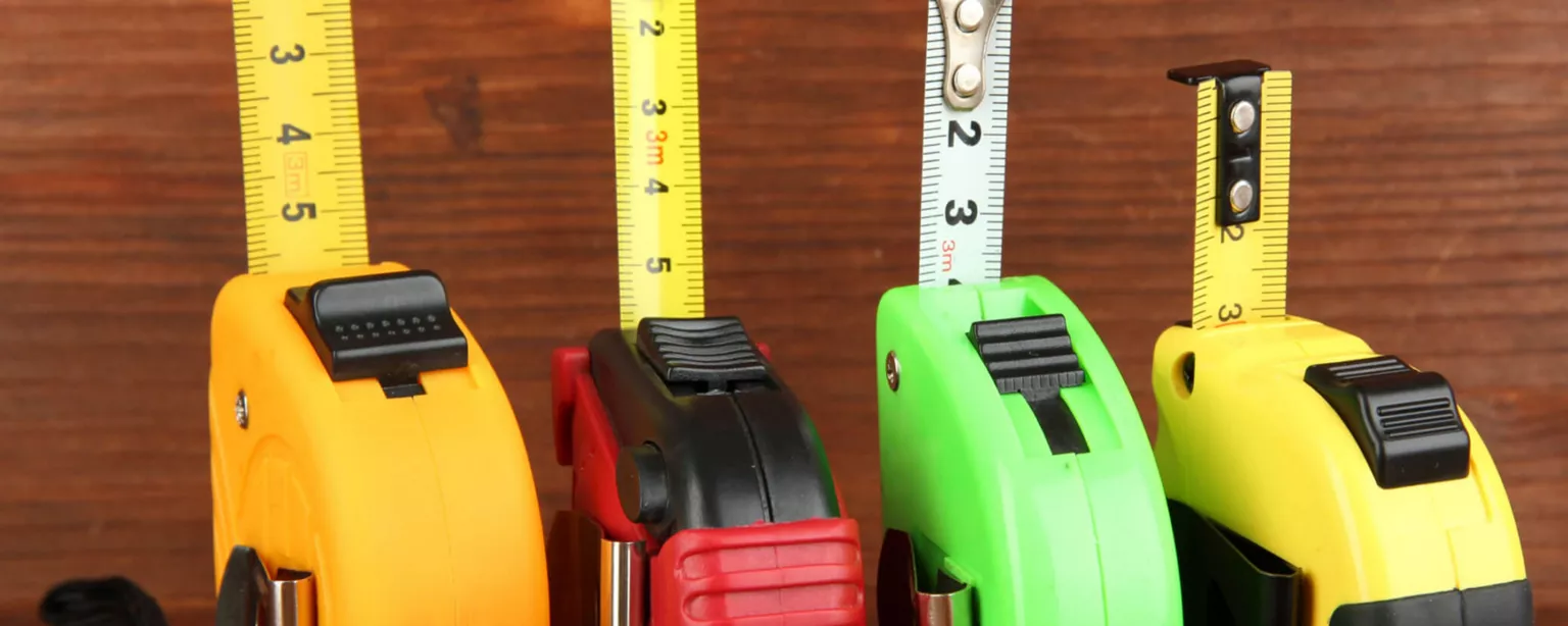 Four tape measures of different sizes and colors showing different measurements against a wooden backdrop.