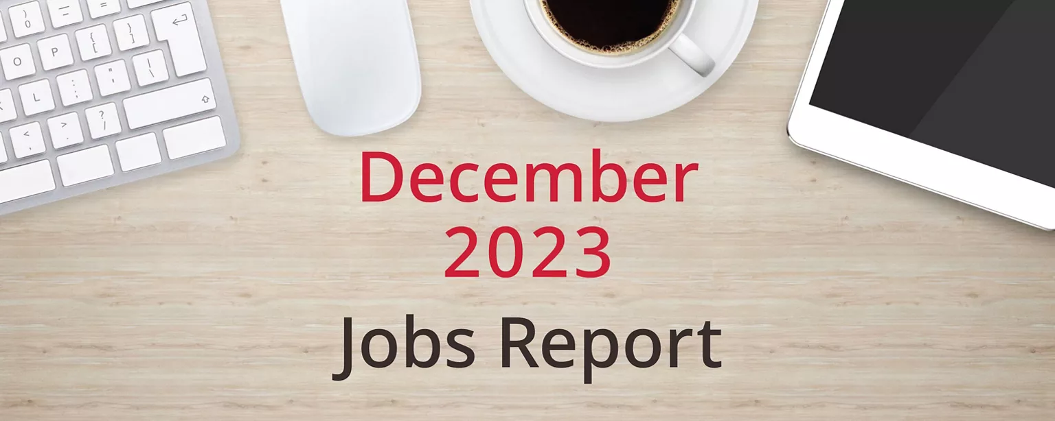 On a wooden desktop, positioned below a keyboard, mouse, cup of coffee and a tablet computer, are the words, “December 2023 Jobs Report.”