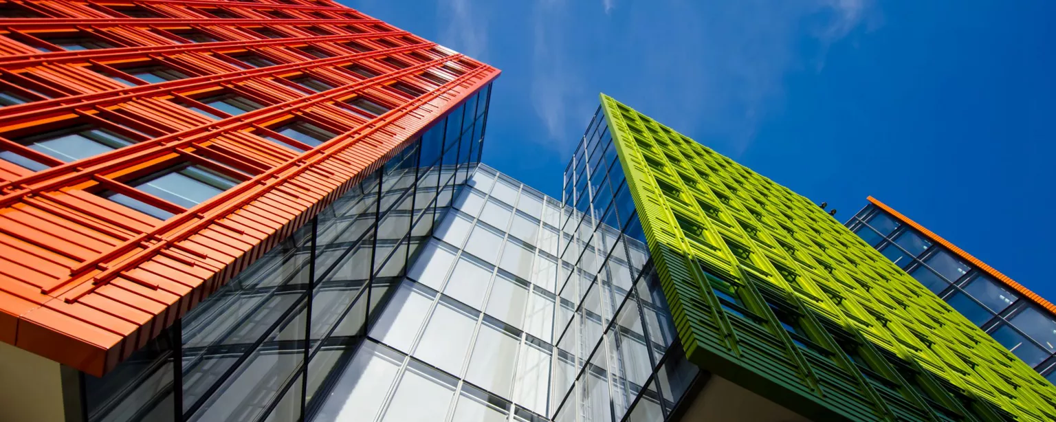 Looking up at three modern office buildings, orange, white and green, with a view toward a blue sky.
