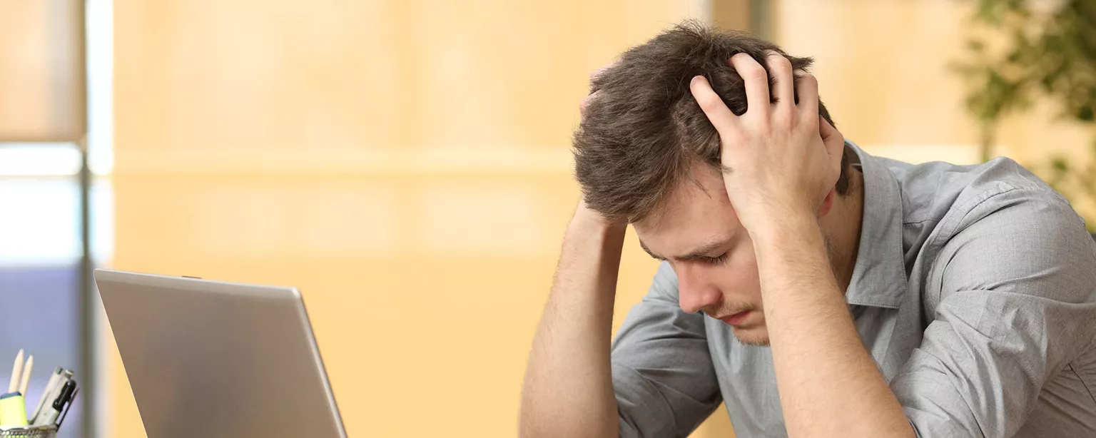 Worker at laptop with head in hands demonstrating lack of employee motivation