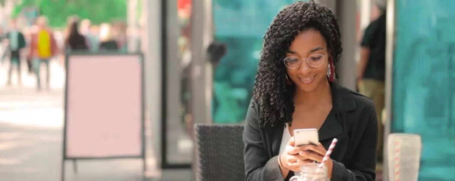 ine junge Frau sitzt vor einem Café und liest erfreut eine Mitteilung auf ihrem Smartphone 
