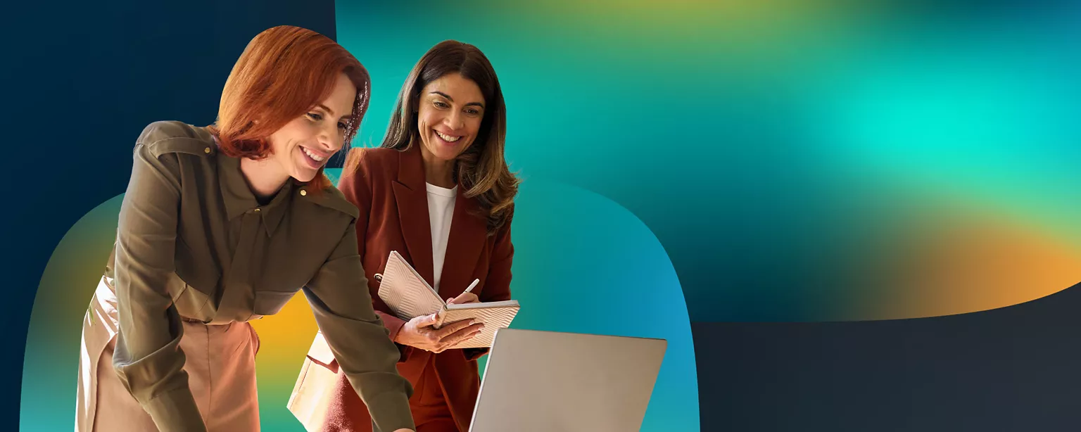 Two women smiling and standing over a computer.
