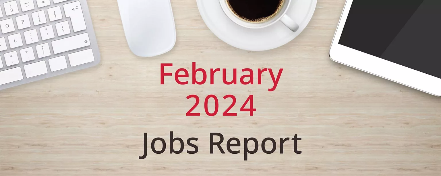 On a wooden desktop, positioned below a keyboard, mouse, cup of coffee and a tablet computer, are the words, “February 2024 Jobs Report.”