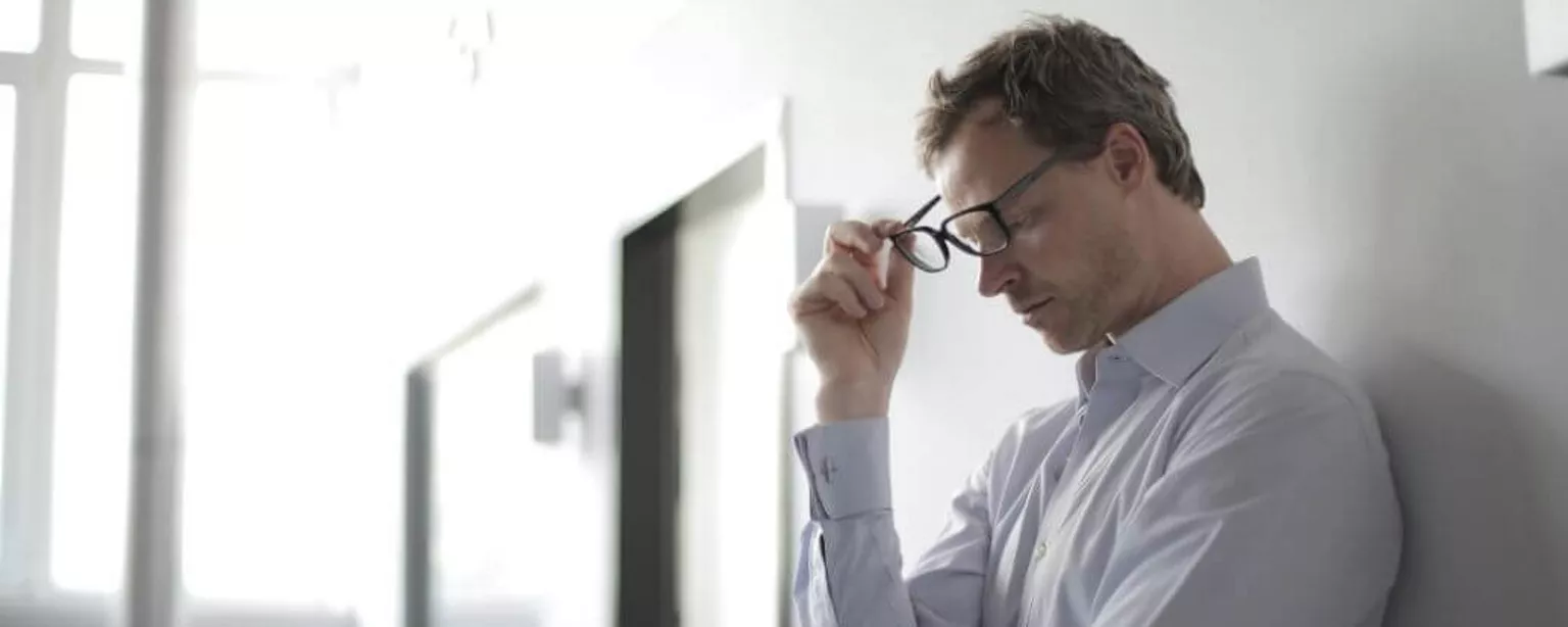 Mann schaut erschöpft und hält schwarze Brille