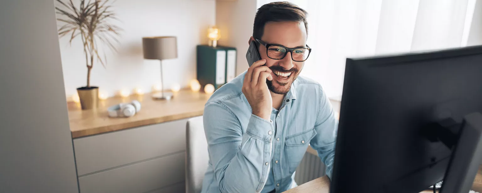 Man on a telephone sits on a computer at home and is happy