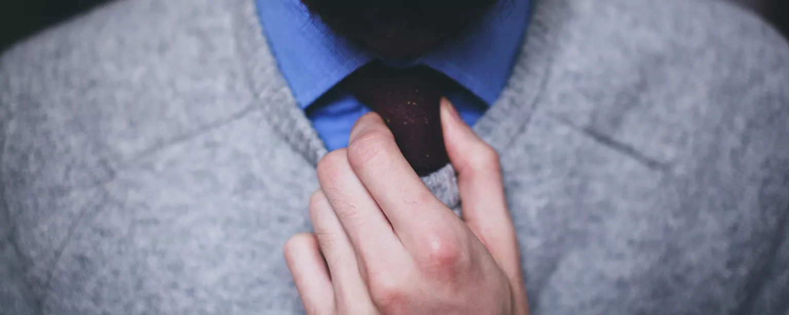 Ein bärtiger Mann im Pullover richtet seinen Krawattenknoten