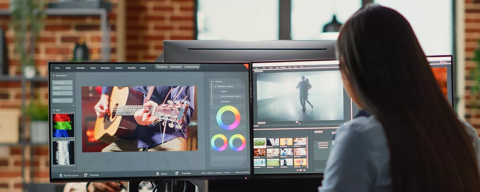 The woman with long dark hair sits in front of two monitors working on designs.