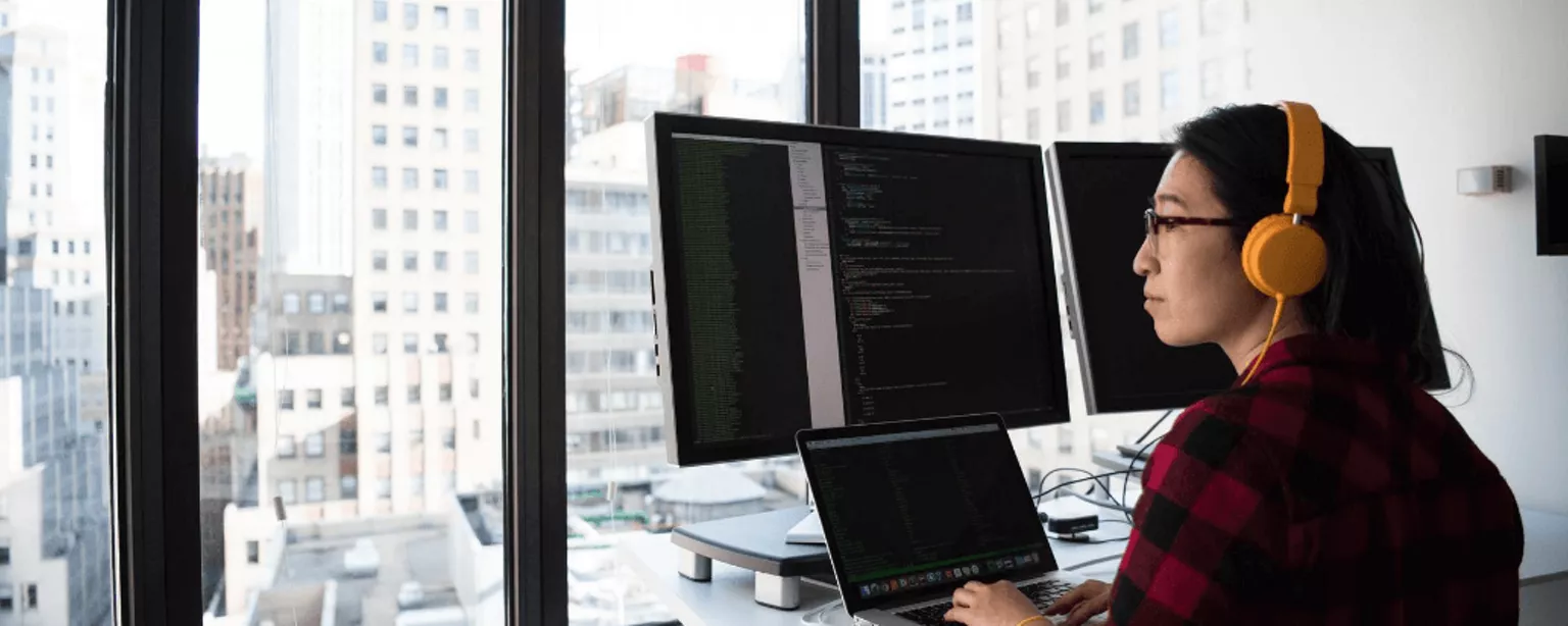 Frau programmiert mit drei Bildschirmen in einem Büro im oberen Stockwerk