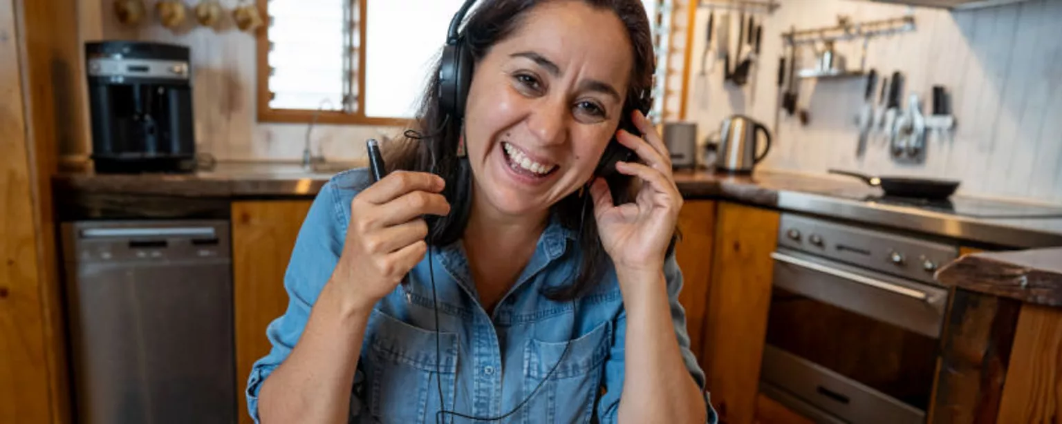 An administrative professional working from her kitchen smiles as she converses using a headset.
