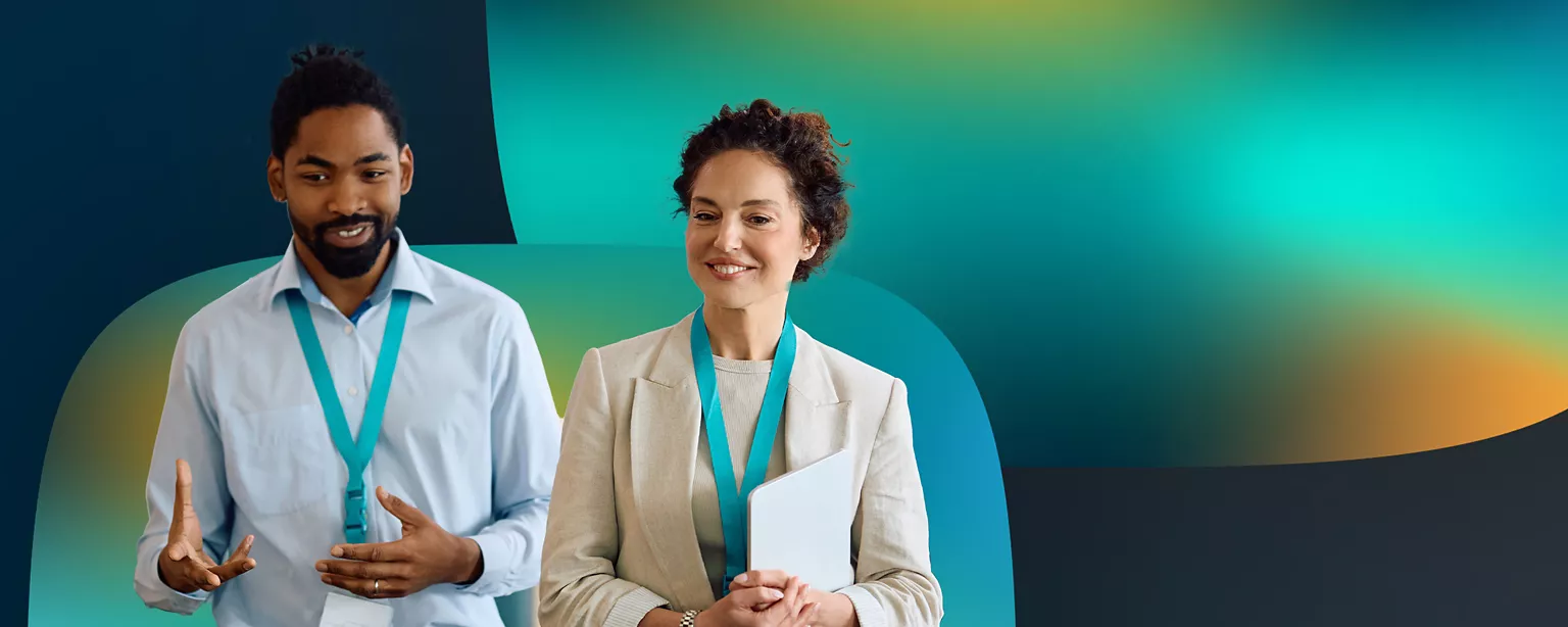 A man and a woman stand next to each other smiling wearing blue lanyards.