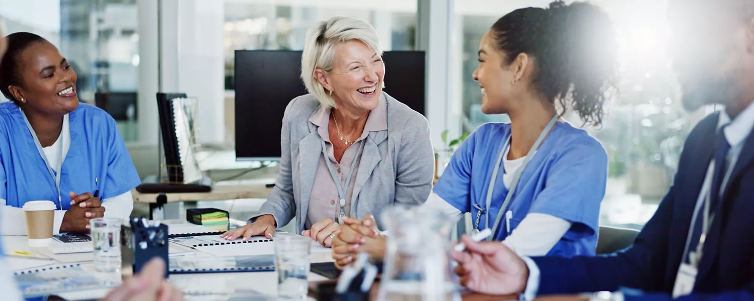 Group of medical professionals sit around a table smiling at each other.