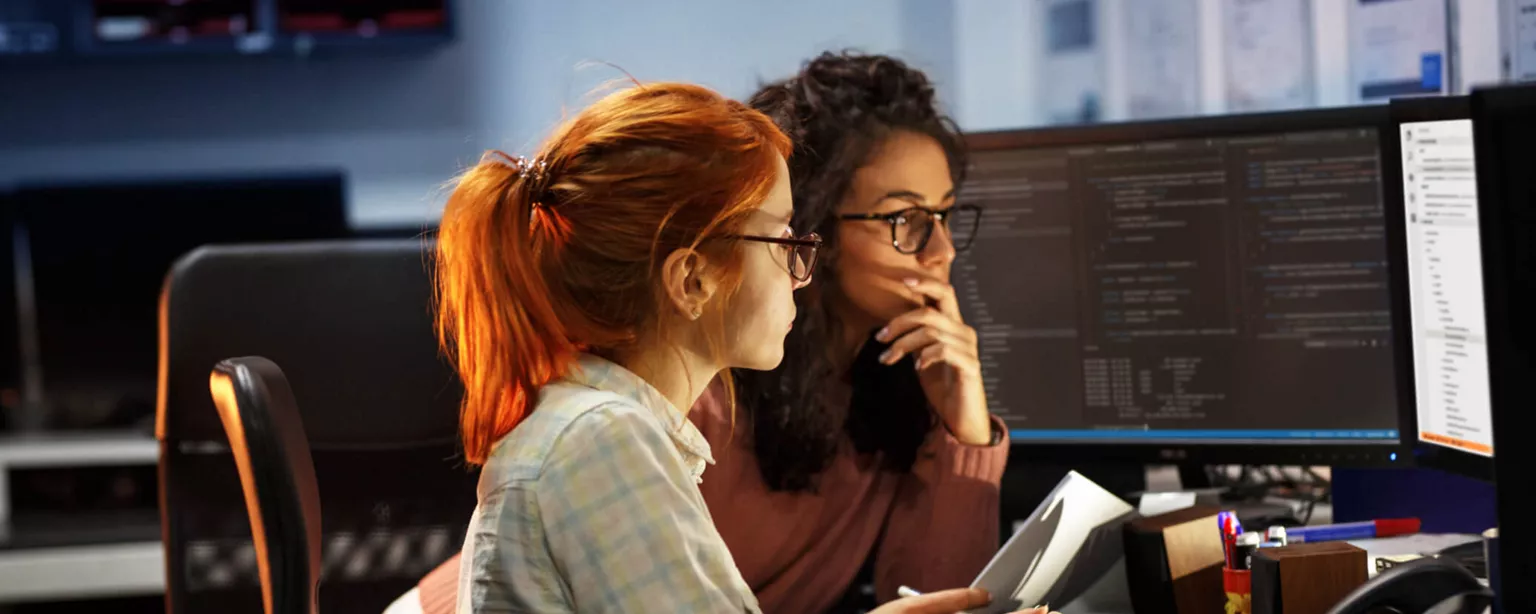 Two female programmers at a desk and looking at a screen.