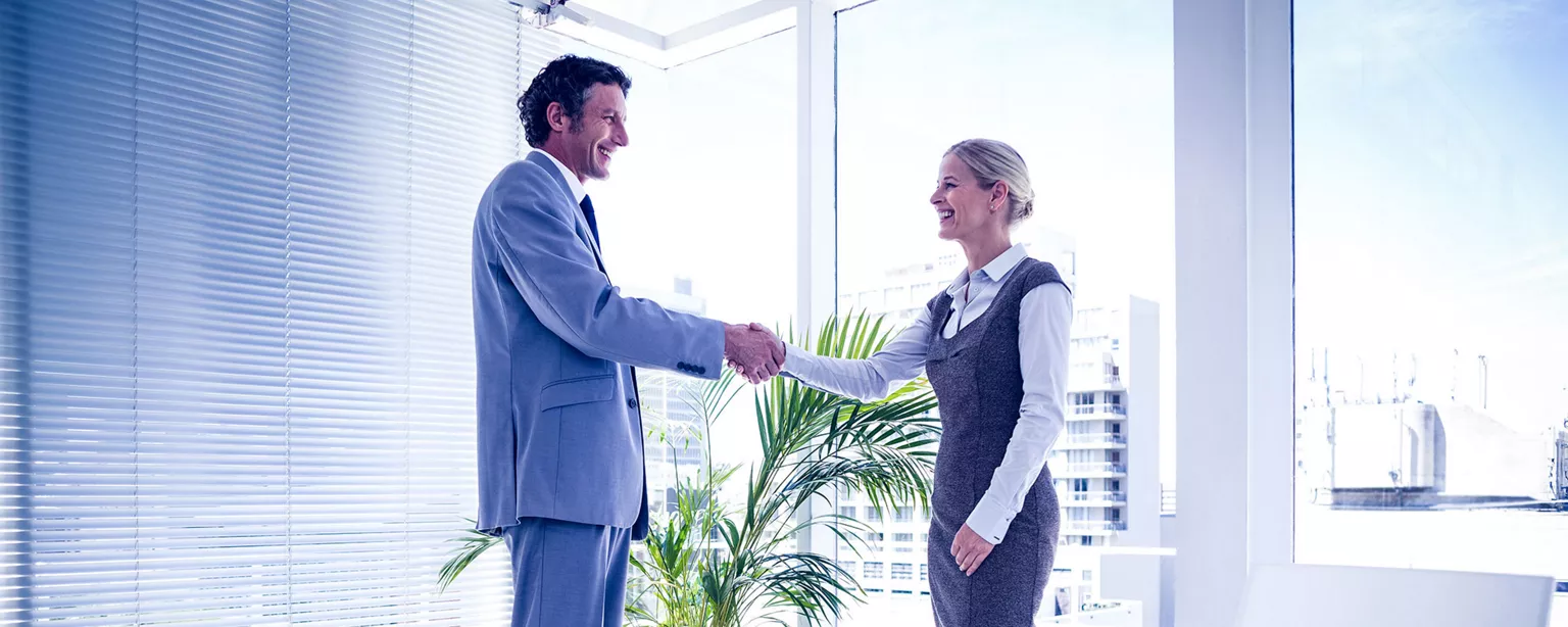 Smiling man and women in office shaking hands at end of hiring process
