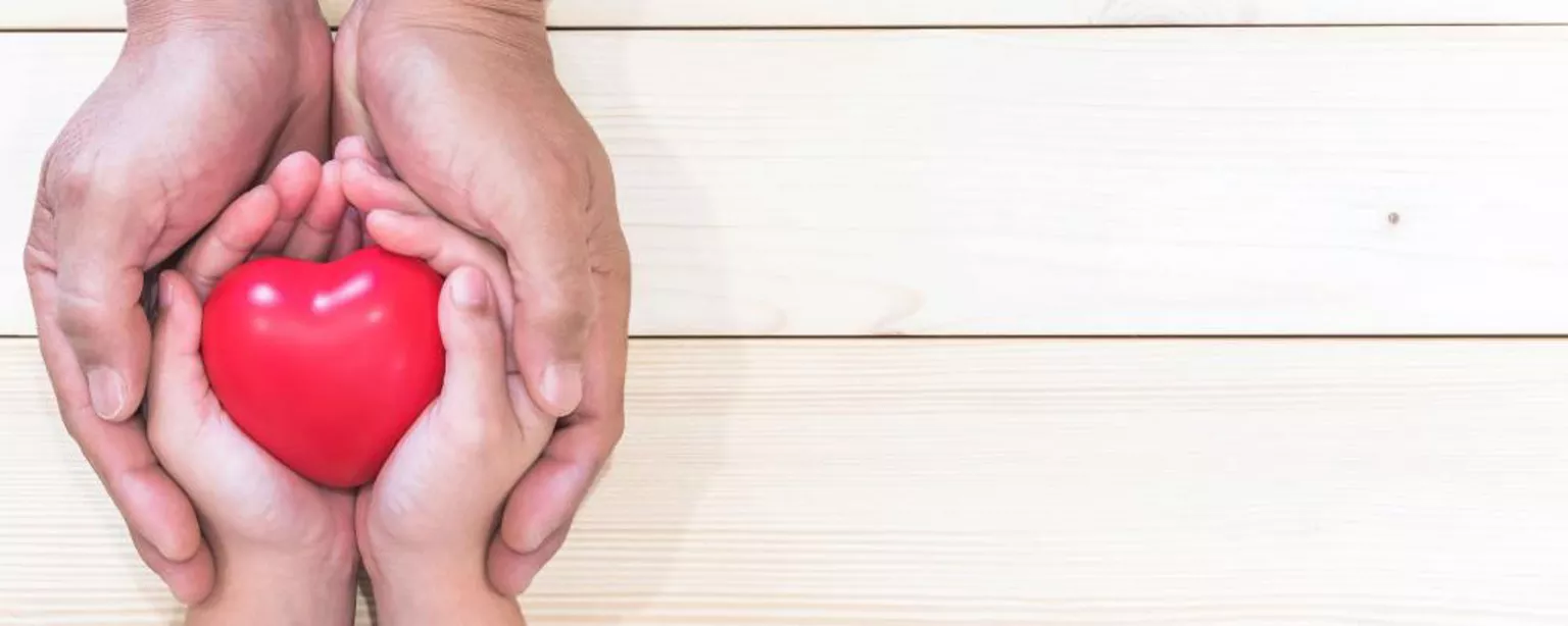 Dons des Fêtes chez Robert Half - un adulte enveloppant les mains d'un enfant qui tient un objet en forme de coeur.