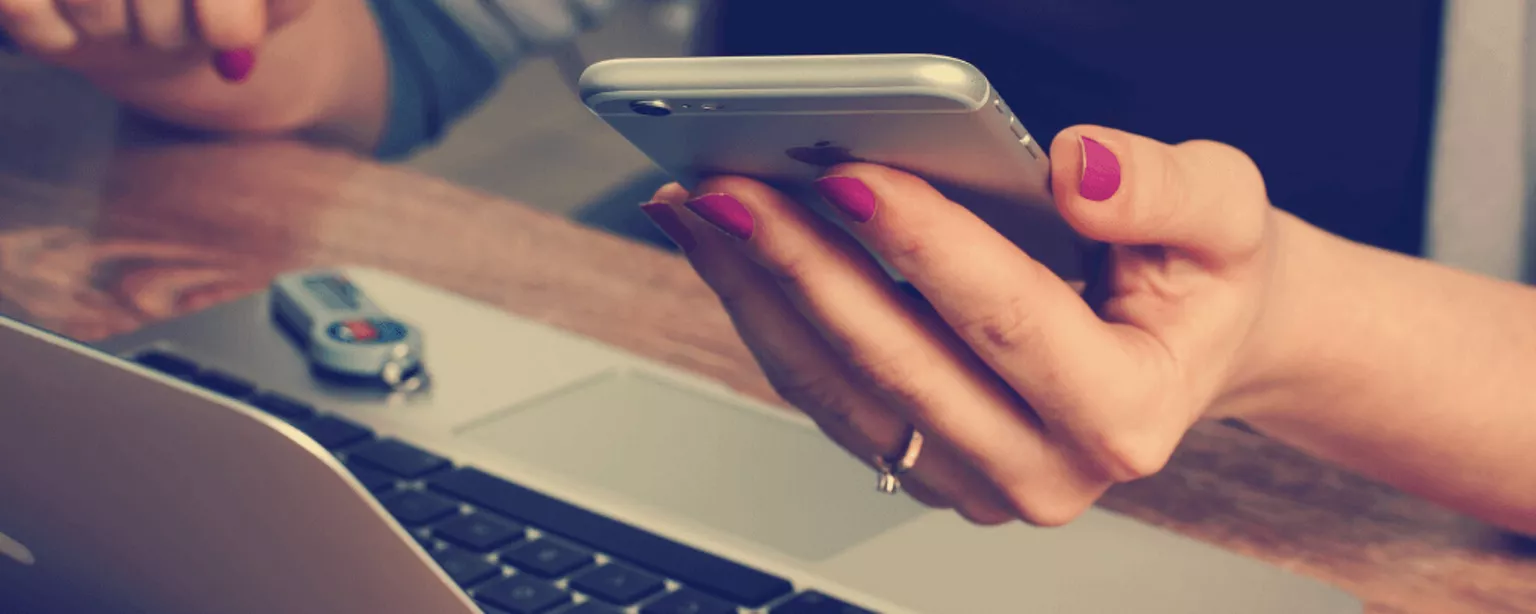 Frau sitzt zuhause vor Laptop mit Handy in der Hand