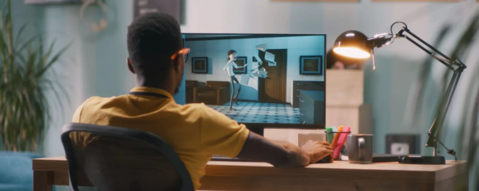 A young man in a yellow shirt and glasses, a 3D animator, workers on a 3D animation project on his computer.