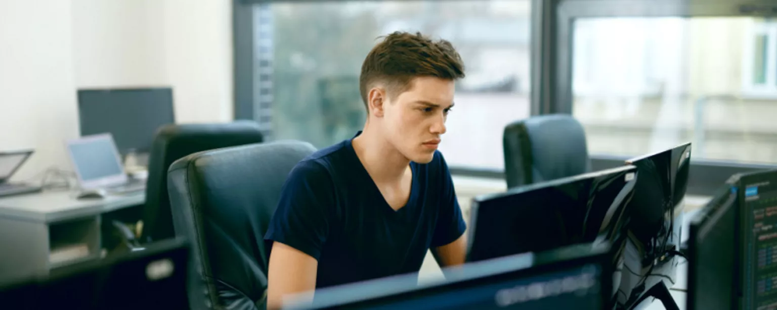 A young man, a front-end web developer, working on a computer and looking at the screen with great concentration.