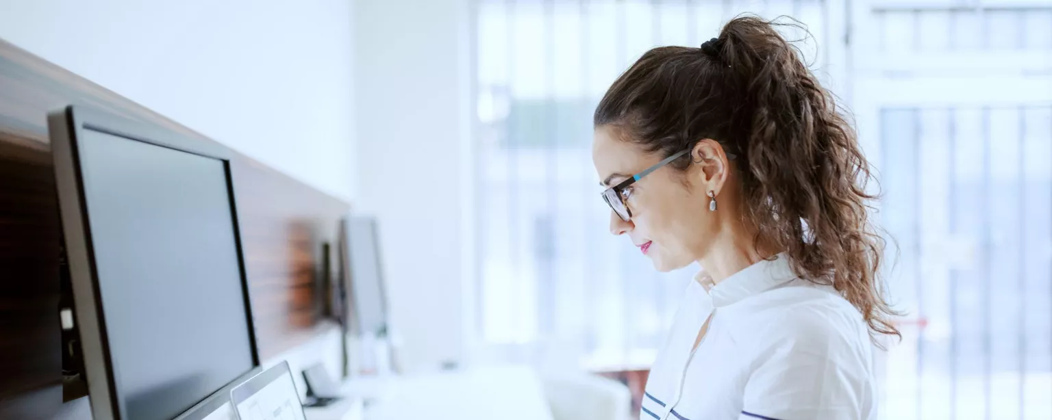 Young woman with a ponytail, glasses and striped sweatshirt, is working intently on a laptop looking at marketing analytics.