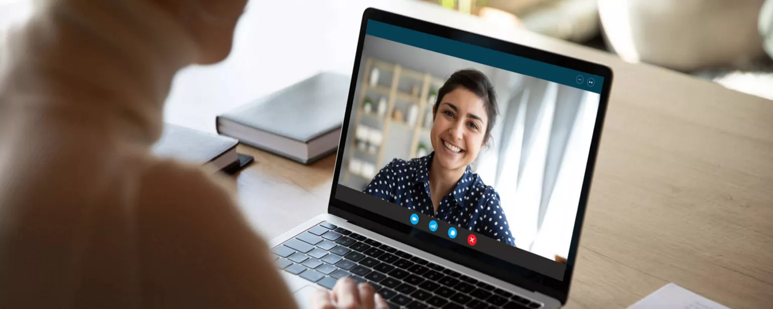 Woman with a hand positioned below her laptop's keyboard talks with a smiling woman on the screen.