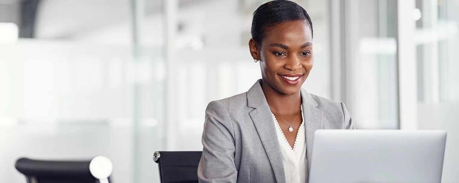 A payroll specialist smiles as she works at her laptop in an office environment.