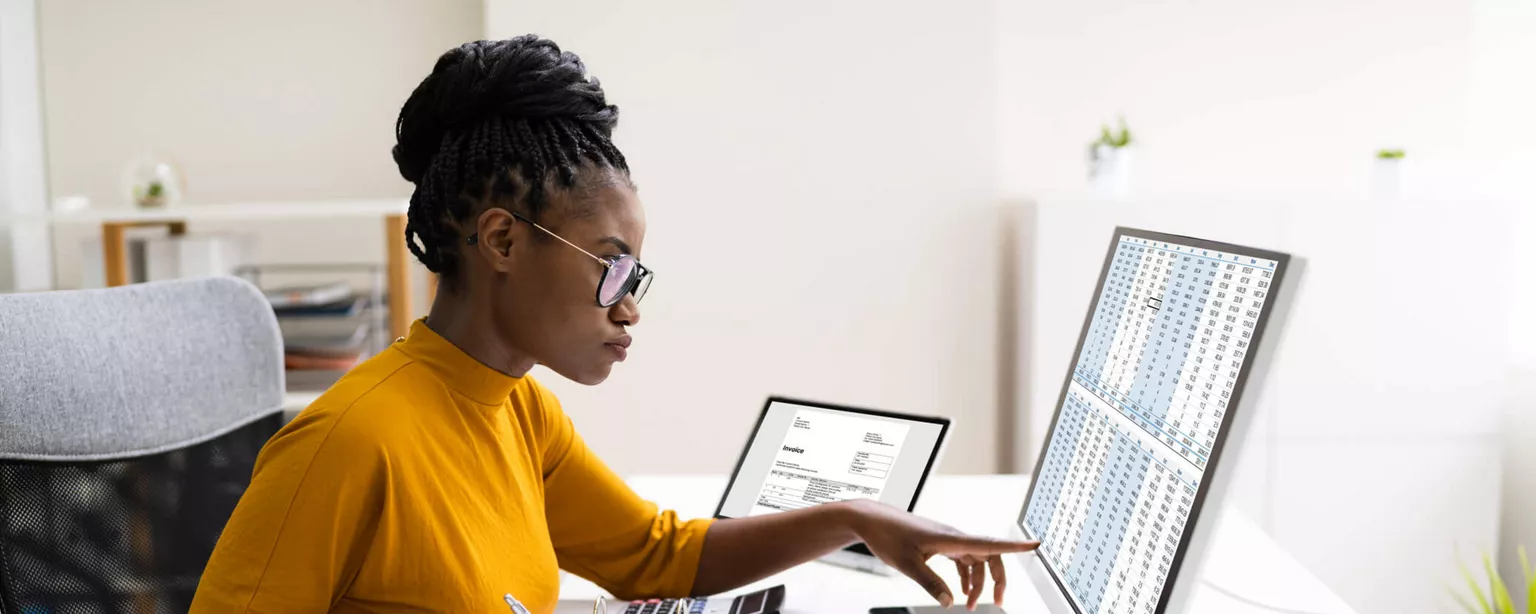 Young woman in a yellow shirt looking at financial figures on a computer screen.