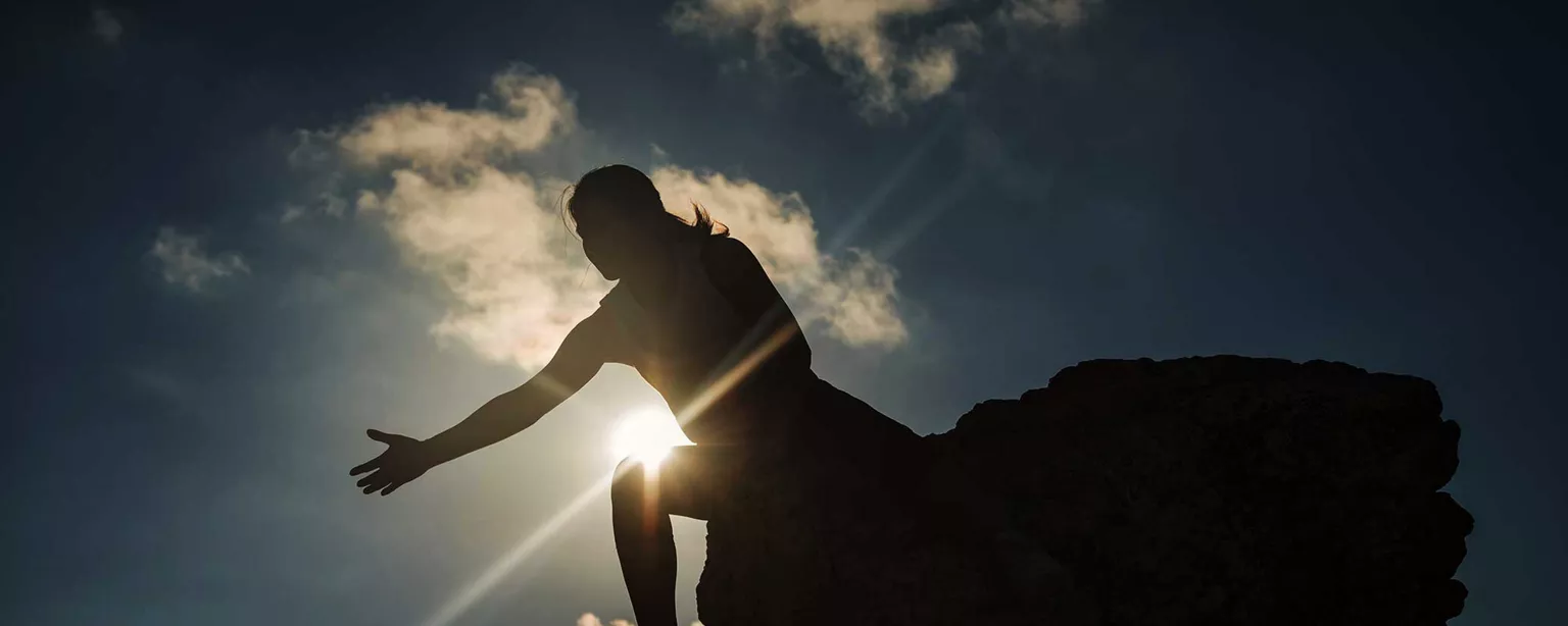 How to Be a Mentor in the Workplace and in Life — woman at top of mountain holding out arm with sun in background