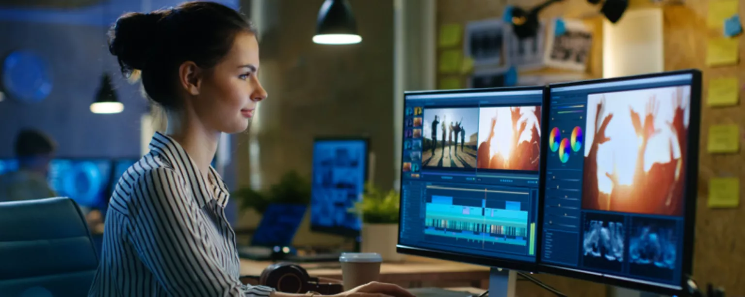 A young woman, a video editor in a creative agency, looking at her video editing work displayed on two computer screens.