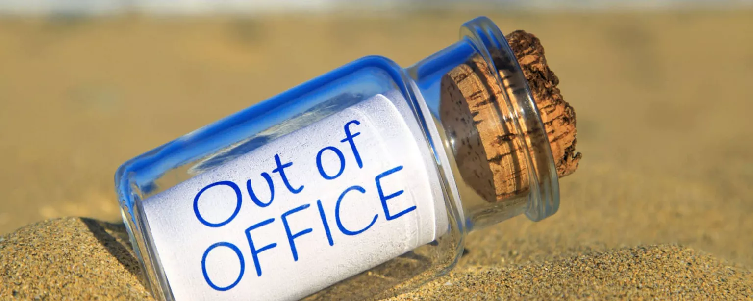 A small corked bottle on a beach has a message inside that reads, "Out of Office."