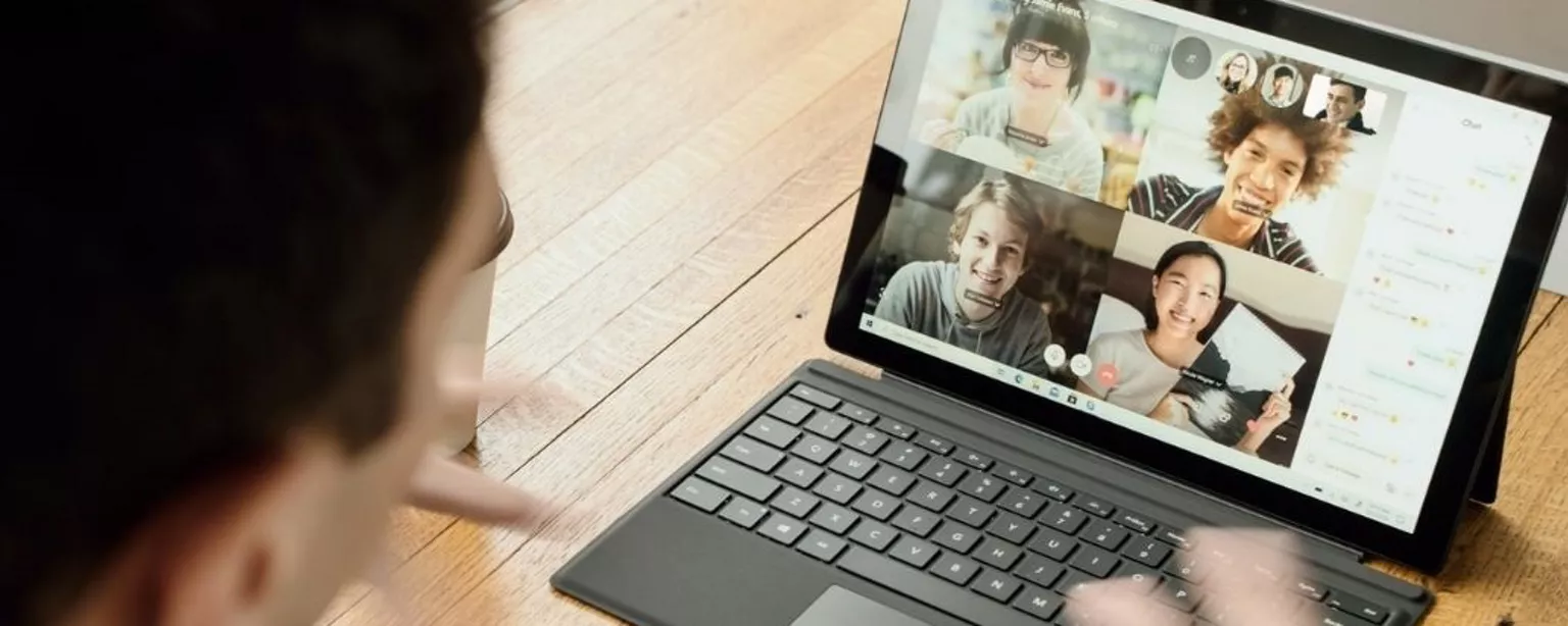 Laptop mit vier Personen in Videocall steht auf einem Tisch