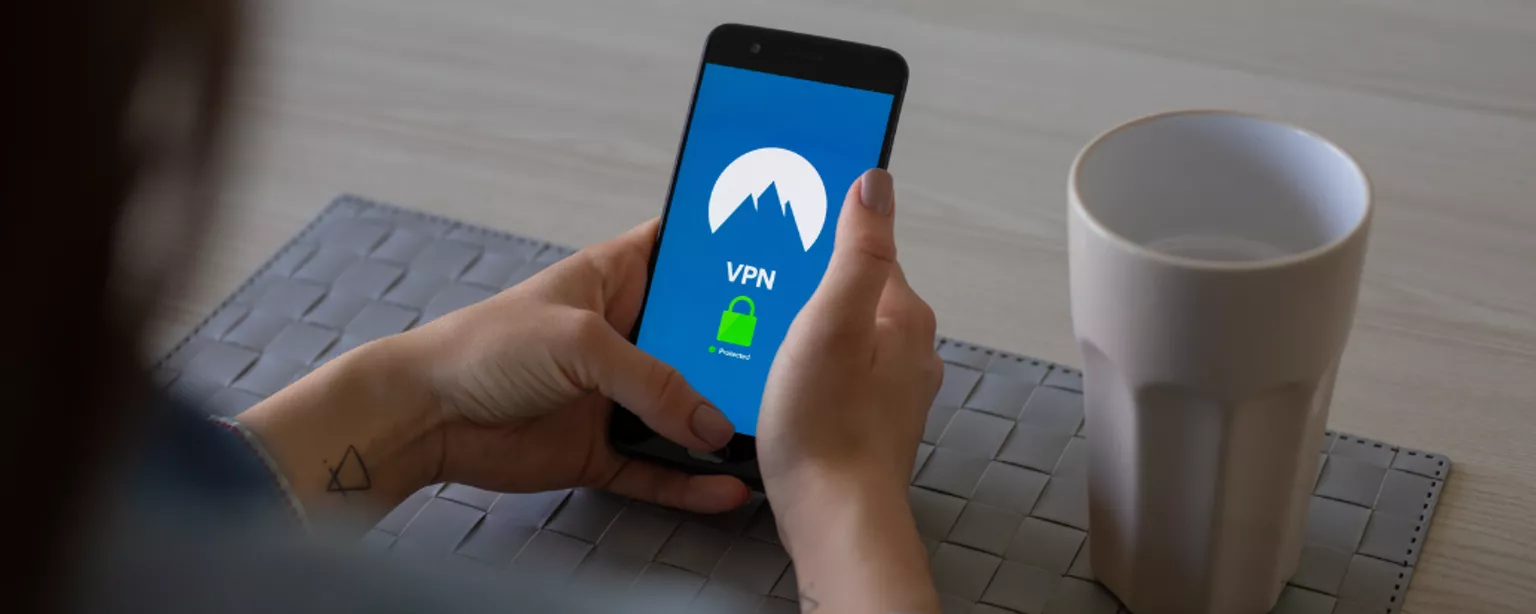 Frau, die ein Smartphone mit VPN-Zeichen darauf in der Hand hält über Keyboard