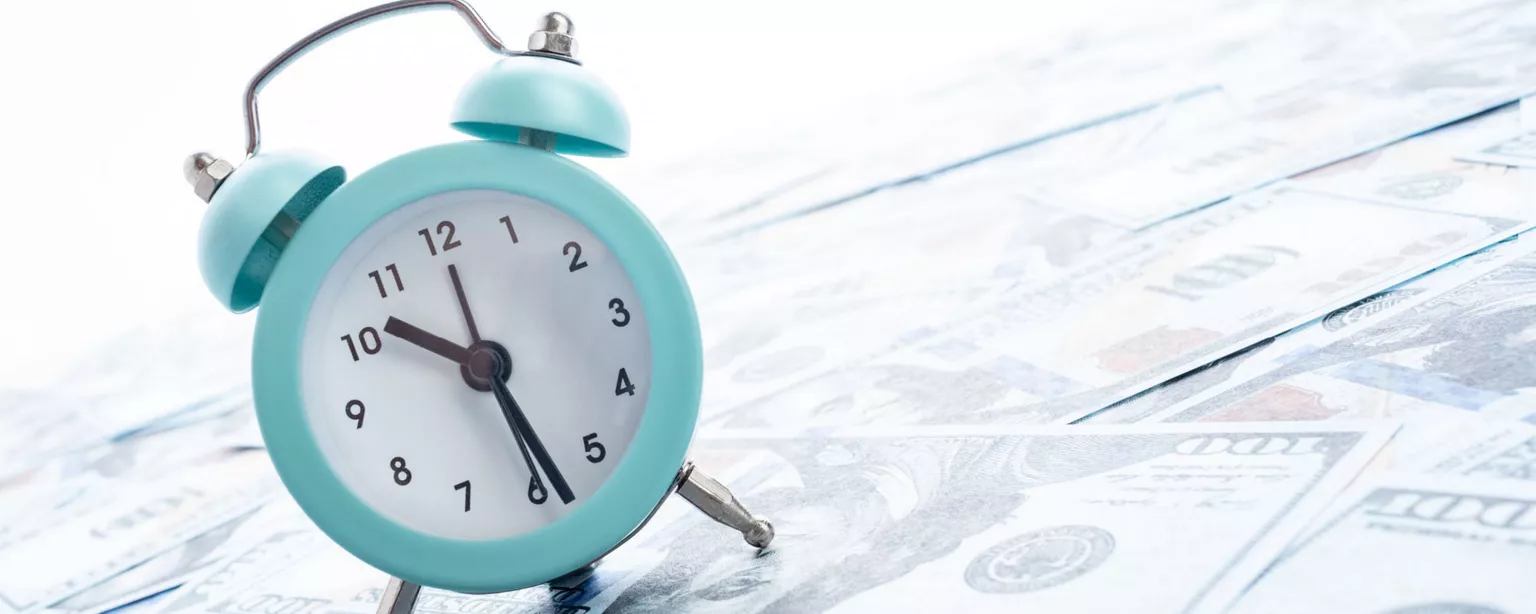 turquoise alarm clock on surface of $100 bills