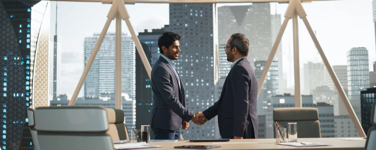 Two men shaking hands in a corporate office at the end of an interview.