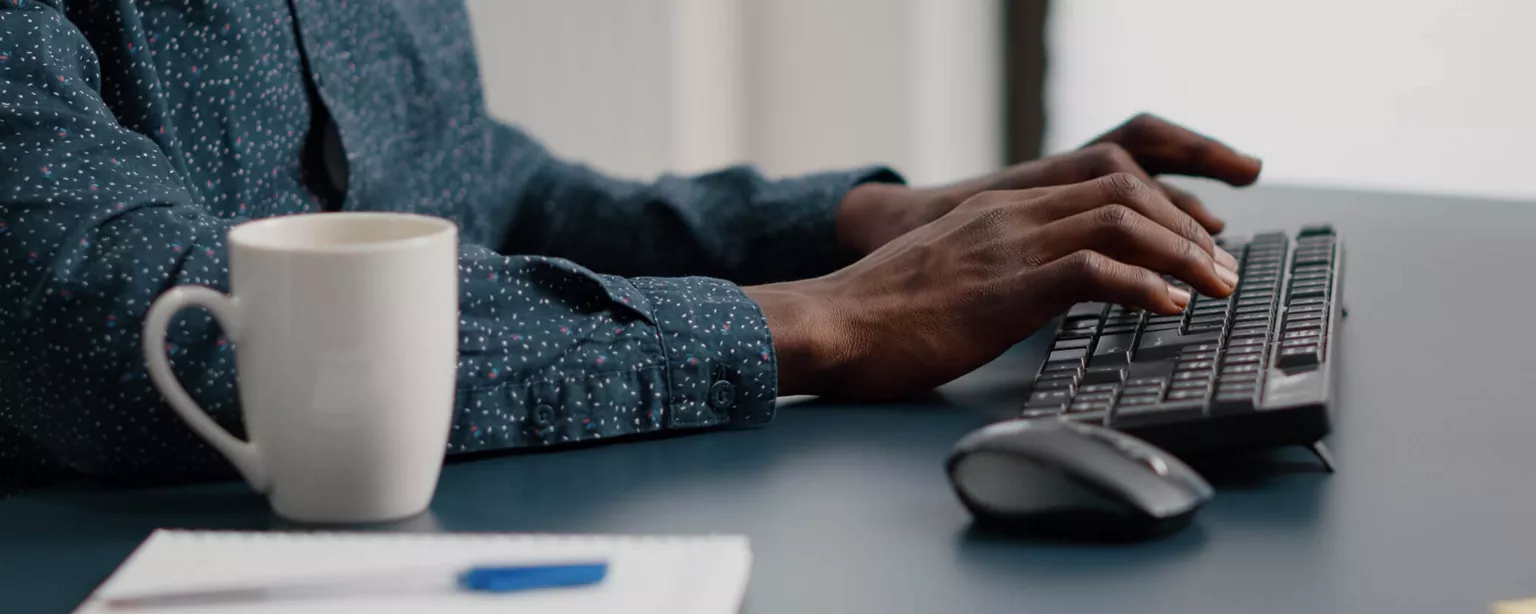 Hiring? Here’s Why You Need to Update Your Job Descriptions — man with hands on keyword next to coffee cup and notebook