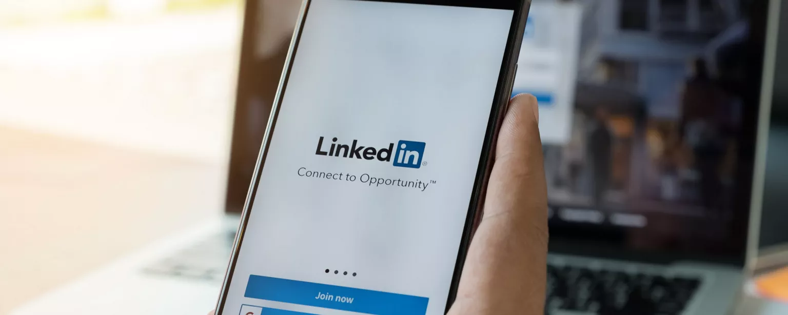A hand holds a mobile phone displaying LinkedIn login page.