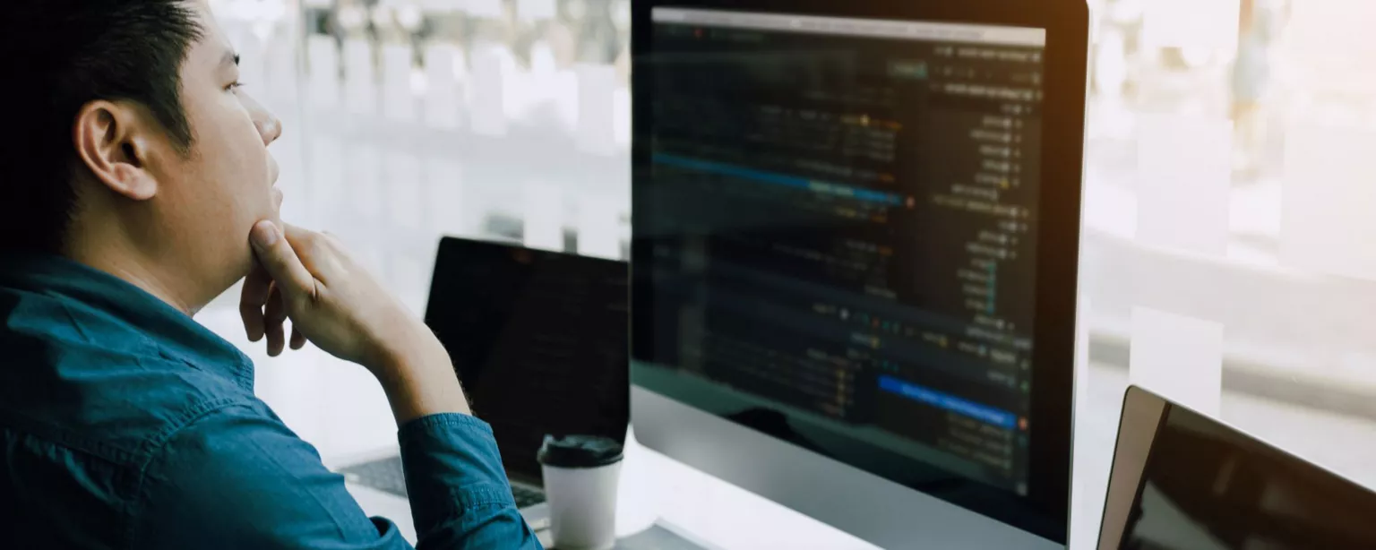 Man in blue shirt looking at computer screens showing code.