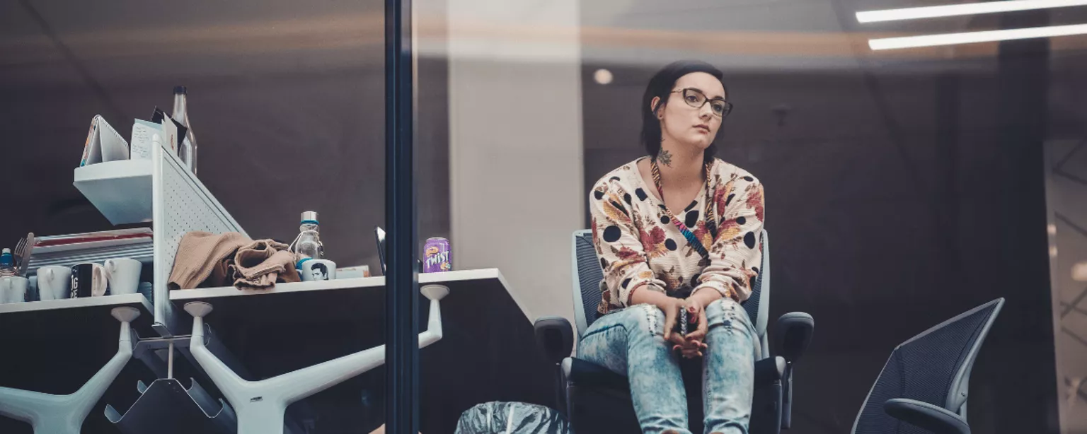 Frau sitzt hinter einer Glasfassade eines Bürogebäudes und guckt nachdenklich 