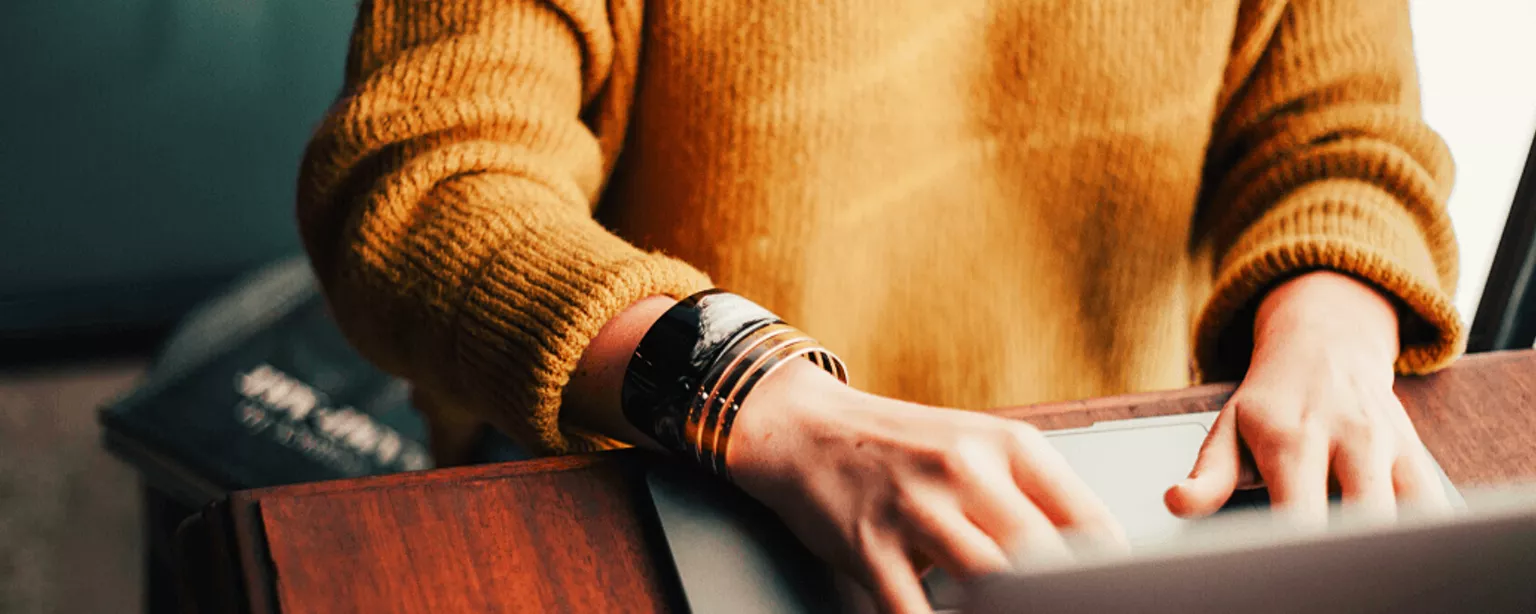 Person sitzt am Tisch und tippt in den Laptop