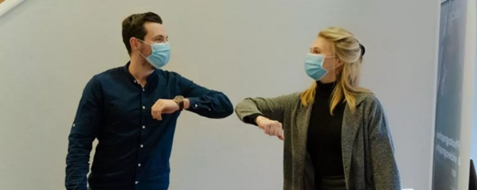 Mann und Frau mit Mundschutz begrüßen sich im Büro per Ellenbogen-Check