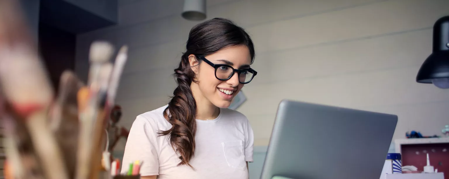 Frau schaut in Ihren Laptop und lächelt