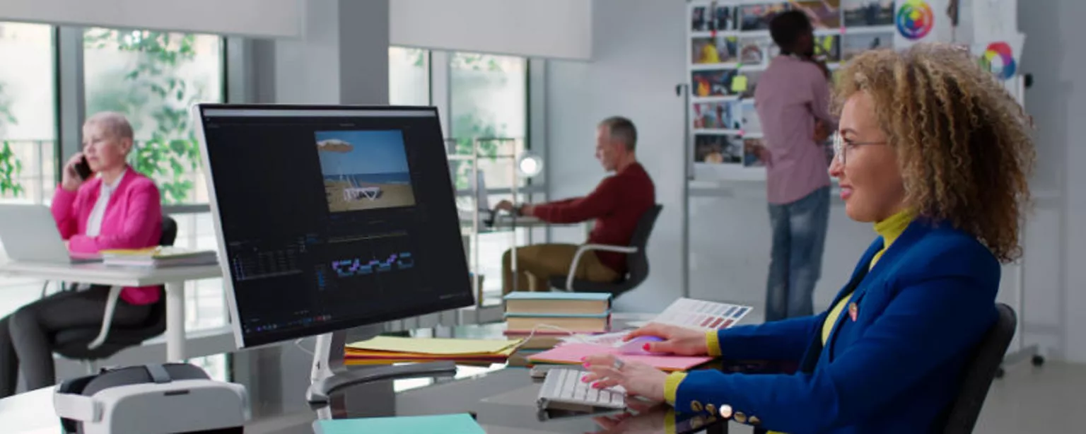A team of people, including a video editor retouching a digital video, is working in a modern creative office.