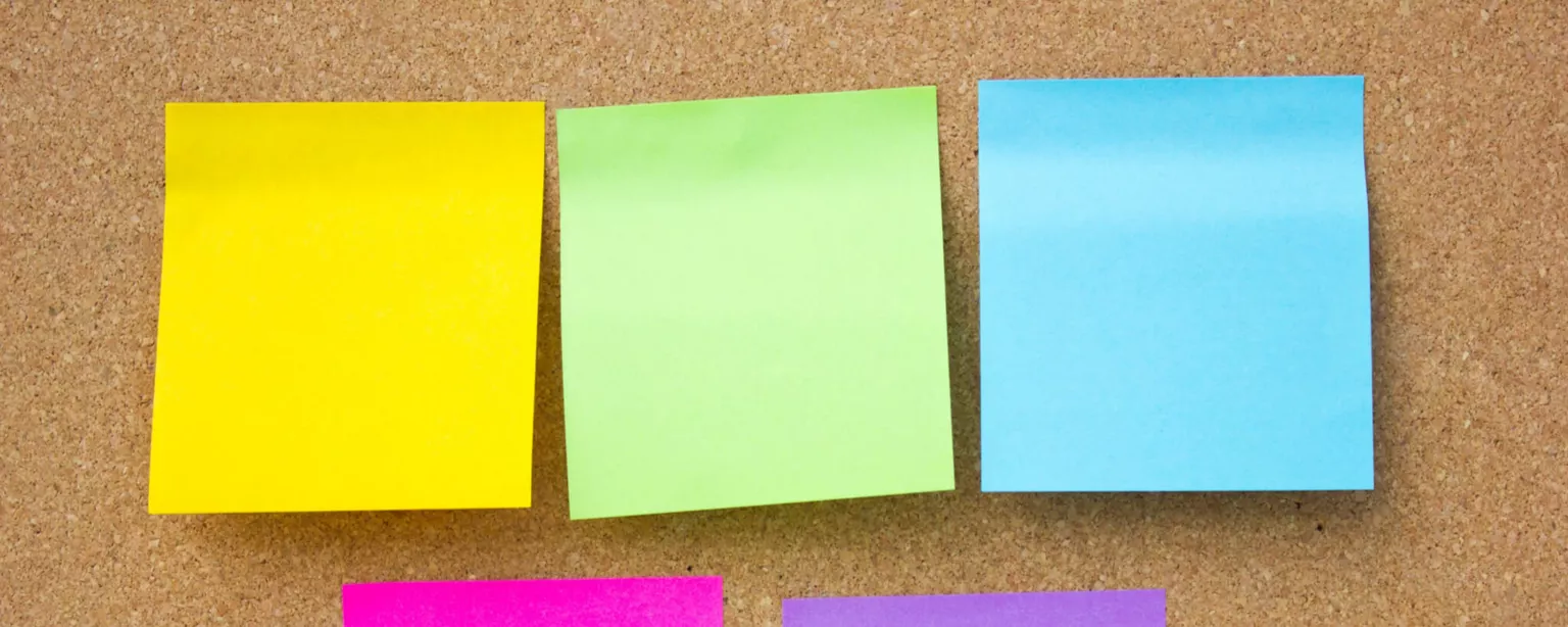 5 blank sticky notes of different colors, adhered to a bulletin board.