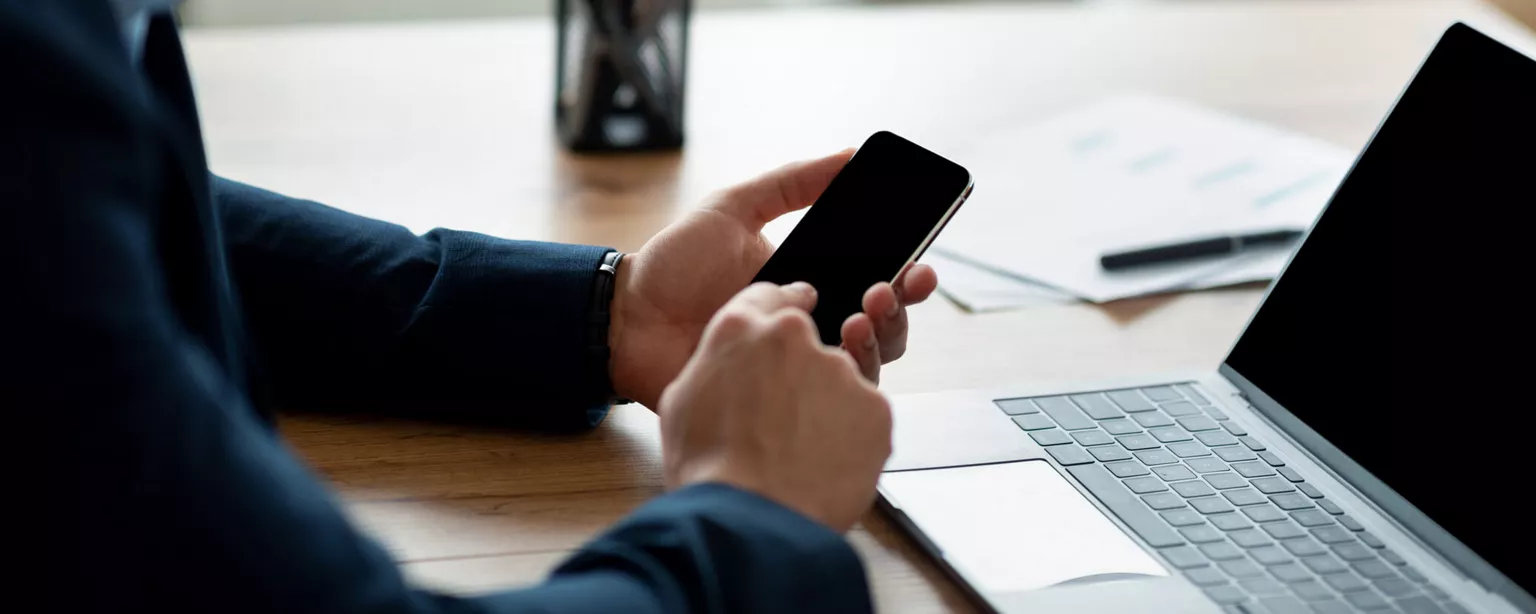 Assessing the Benefits of On-Demand Pay for Employers — man checks phone app at office desk desk