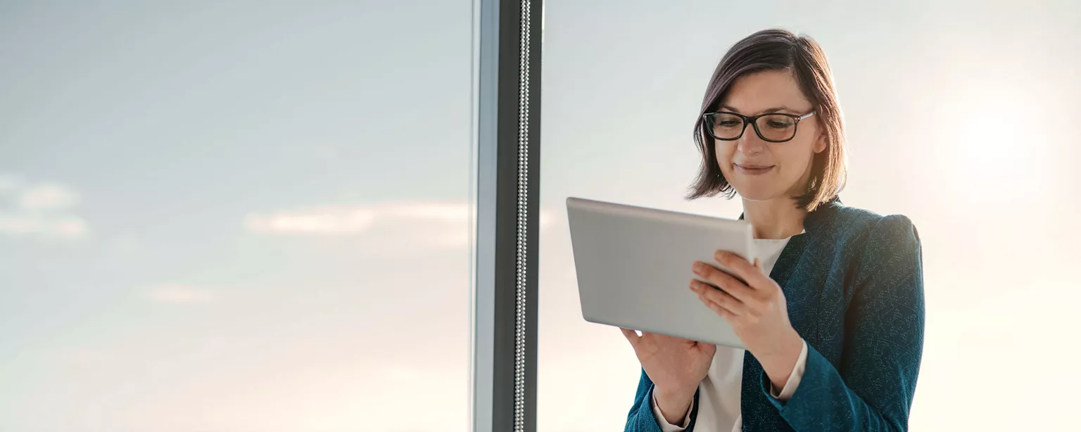Woman standing near window with tablet working as a payroll manager