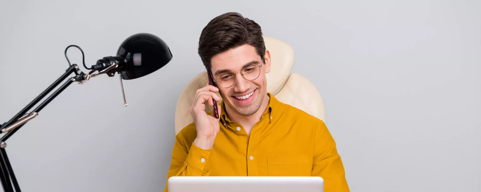5 Post-Pandemic Job Interview Questions — man in yellow shirt talks on the phone with laptop at office desk