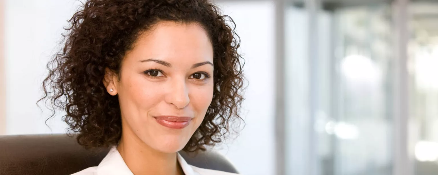 Young businesswoman in a white blazer, sitting in an executive chair and smiling.