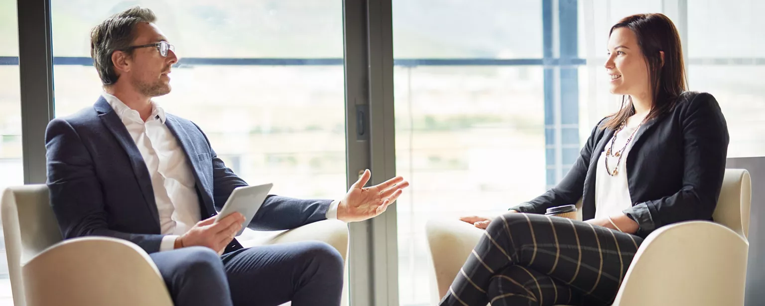 A manager is talking one to one with an employee in an office lounge. Their discussion is a career conversation.