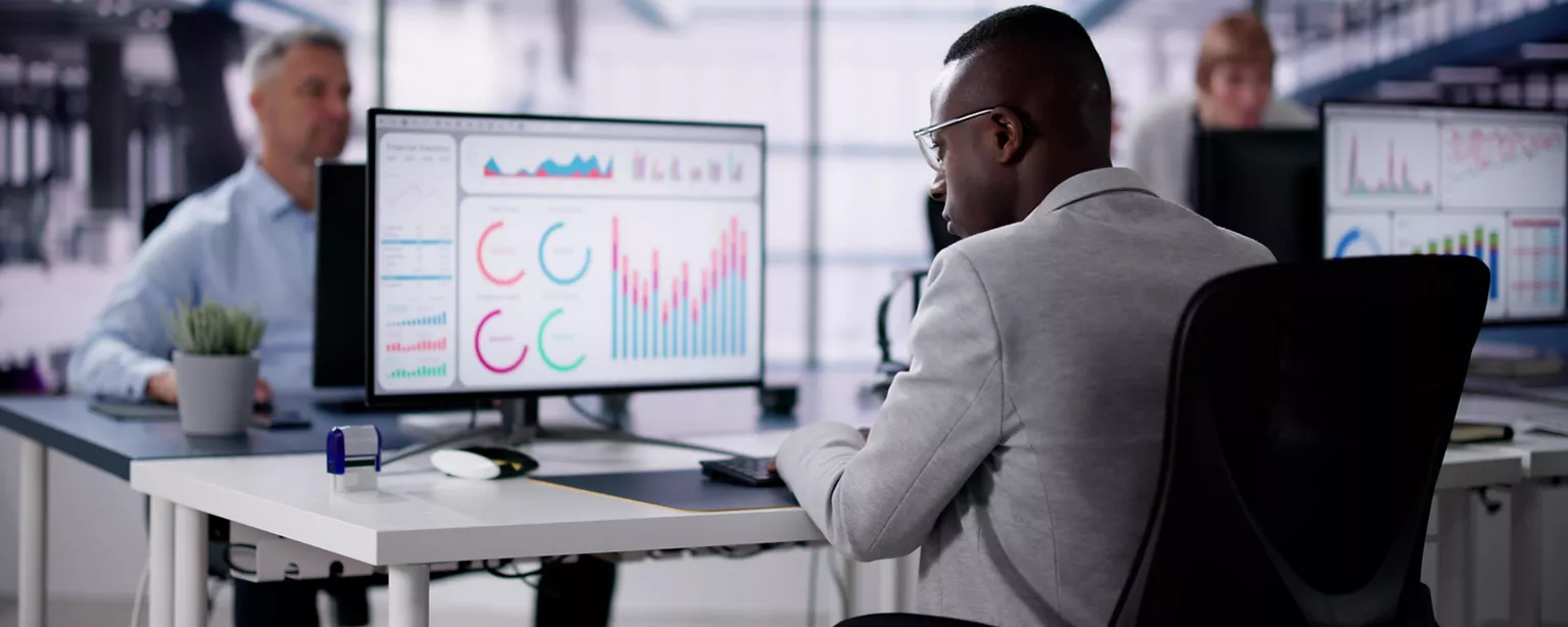 Members of a finance team at their workstations are analyzing data displayed on ERP dashboards on their computer screens.